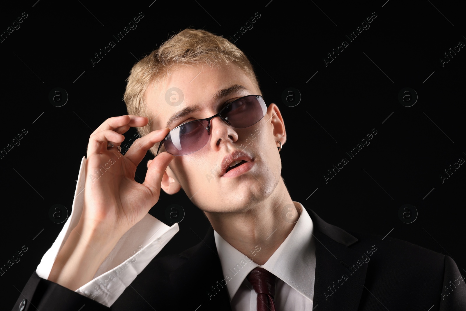 Photo of Handsome young man wearing stylish suit and sunglasses on black background