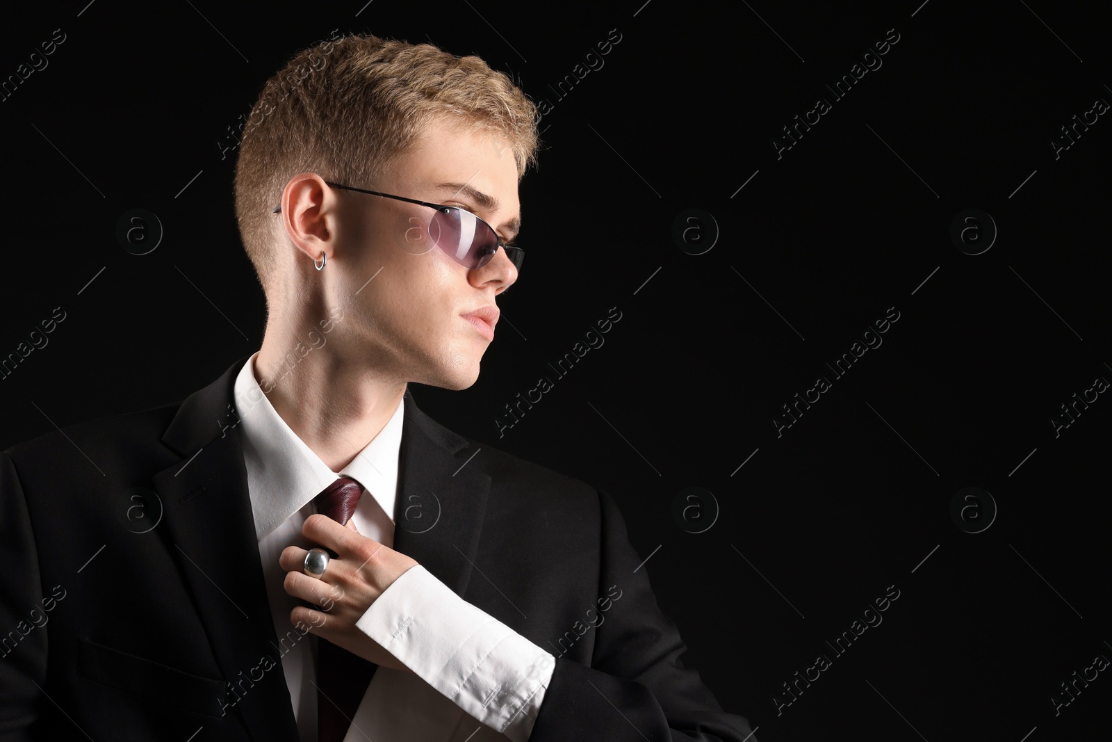 Photo of Handsome young man wearing stylish suit and sunglasses on black background