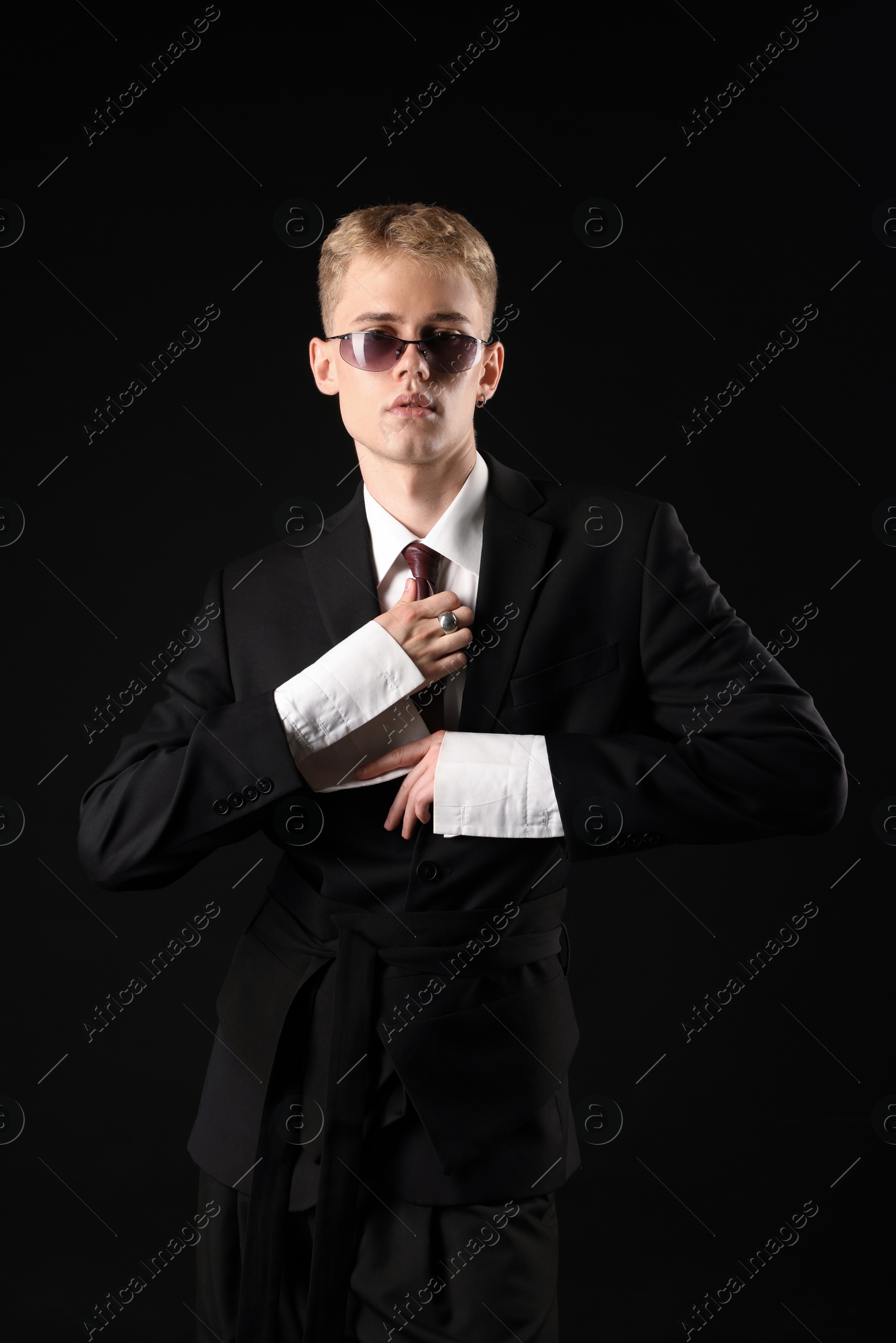 Photo of Handsome young man wearing stylish suit and sunglasses on black background