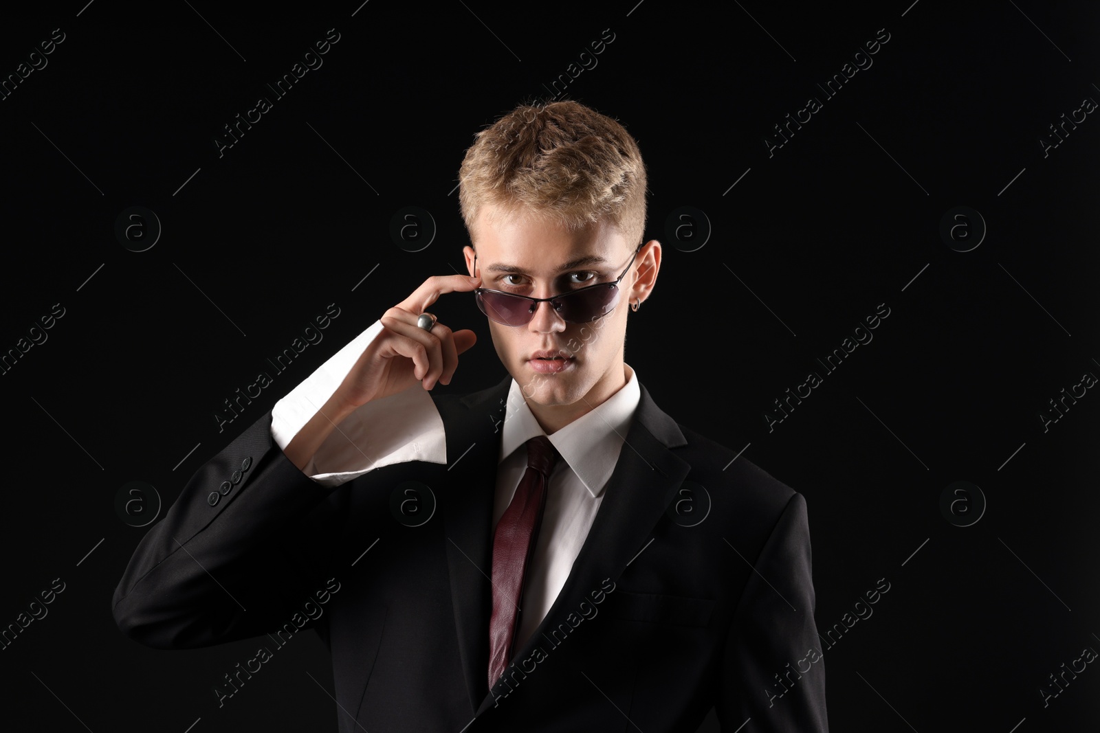 Photo of Handsome young man wearing stylish suit and sunglasses on black background