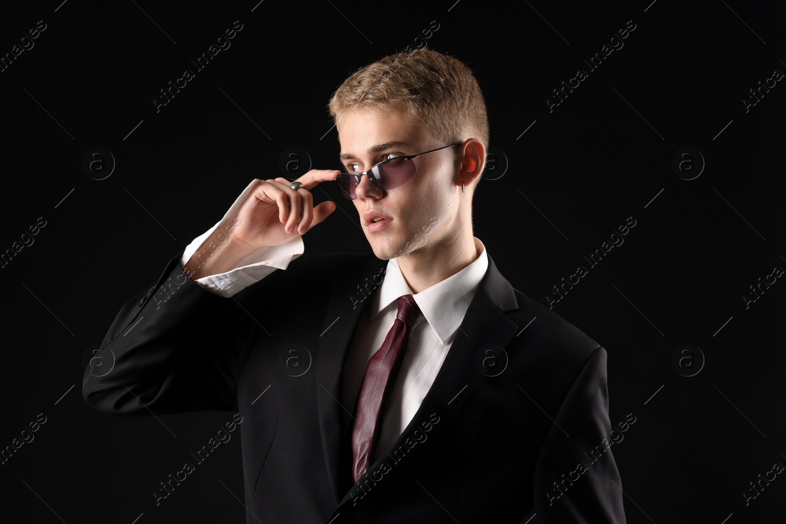 Photo of Handsome young man wearing stylish suit and sunglasses on black background