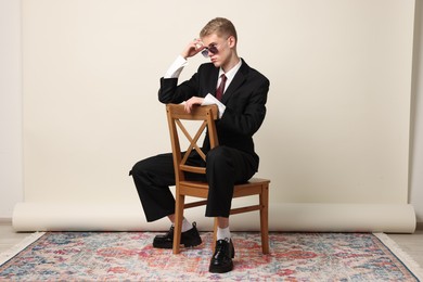 Photo of Handsome young man wearing stylish suit and sunglasses sitting on chair against white background