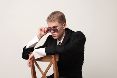 Photo of Handsome young man wearing stylish suit and sunglasses sitting on chair against white background
