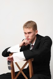 Photo of Handsome young man wearing stylish suit sitting on chair against white background