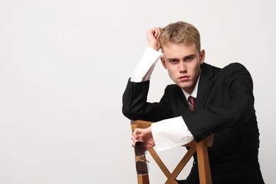 Photo of Handsome young man wearing stylish suit sitting on chair against white background, space for text