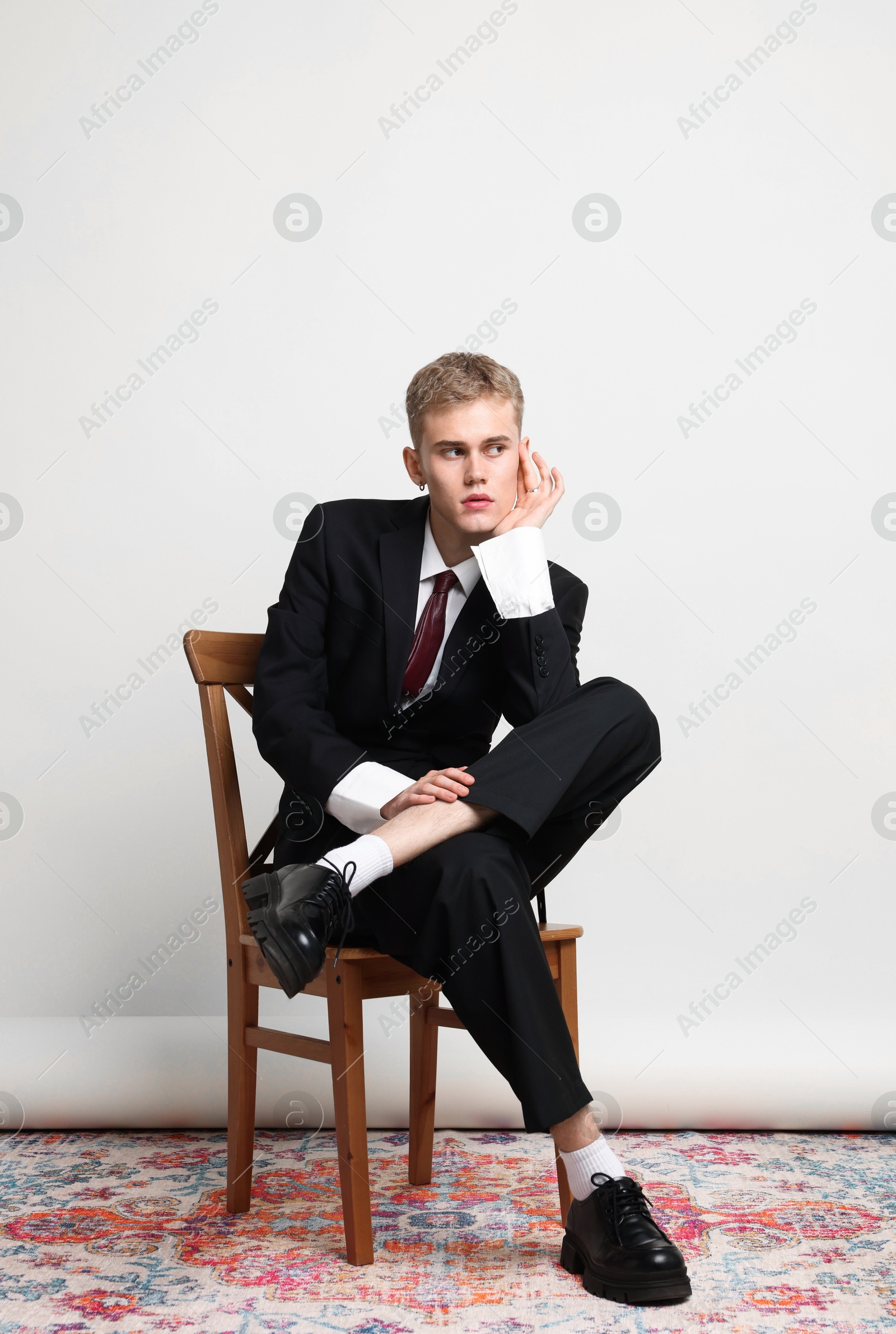 Photo of Handsome young man wearing stylish suit sitting on chair against white background