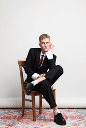 Photo of Handsome young man wearing stylish suit sitting on chair against white background