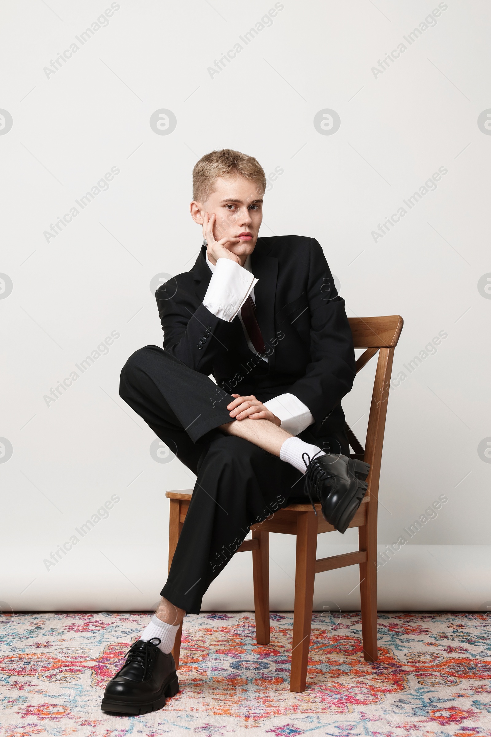 Photo of Handsome young man wearing stylish suit sitting on chair against white background