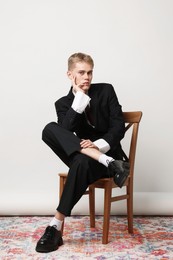 Photo of Handsome young man wearing stylish suit sitting on chair against white background