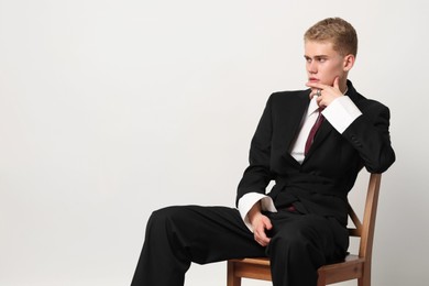 Photo of Handsome young man wearing stylish suit sitting on chair against white background, space for text