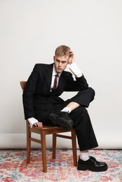 Photo of Handsome young man wearing stylish suit sitting on chair against white background