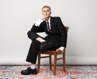 Photo of Handsome young man wearing stylish suit sitting on chair against white background