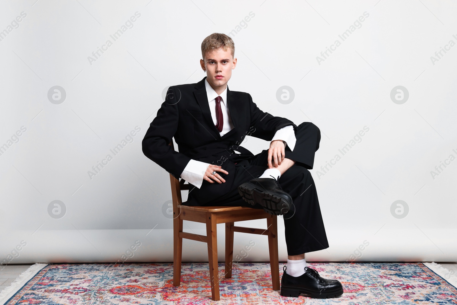Photo of Handsome young man wearing stylish suit sitting on chair against white background