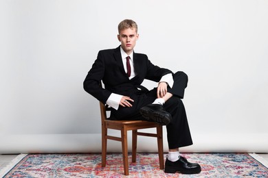 Photo of Handsome young man wearing stylish suit sitting on chair against white background