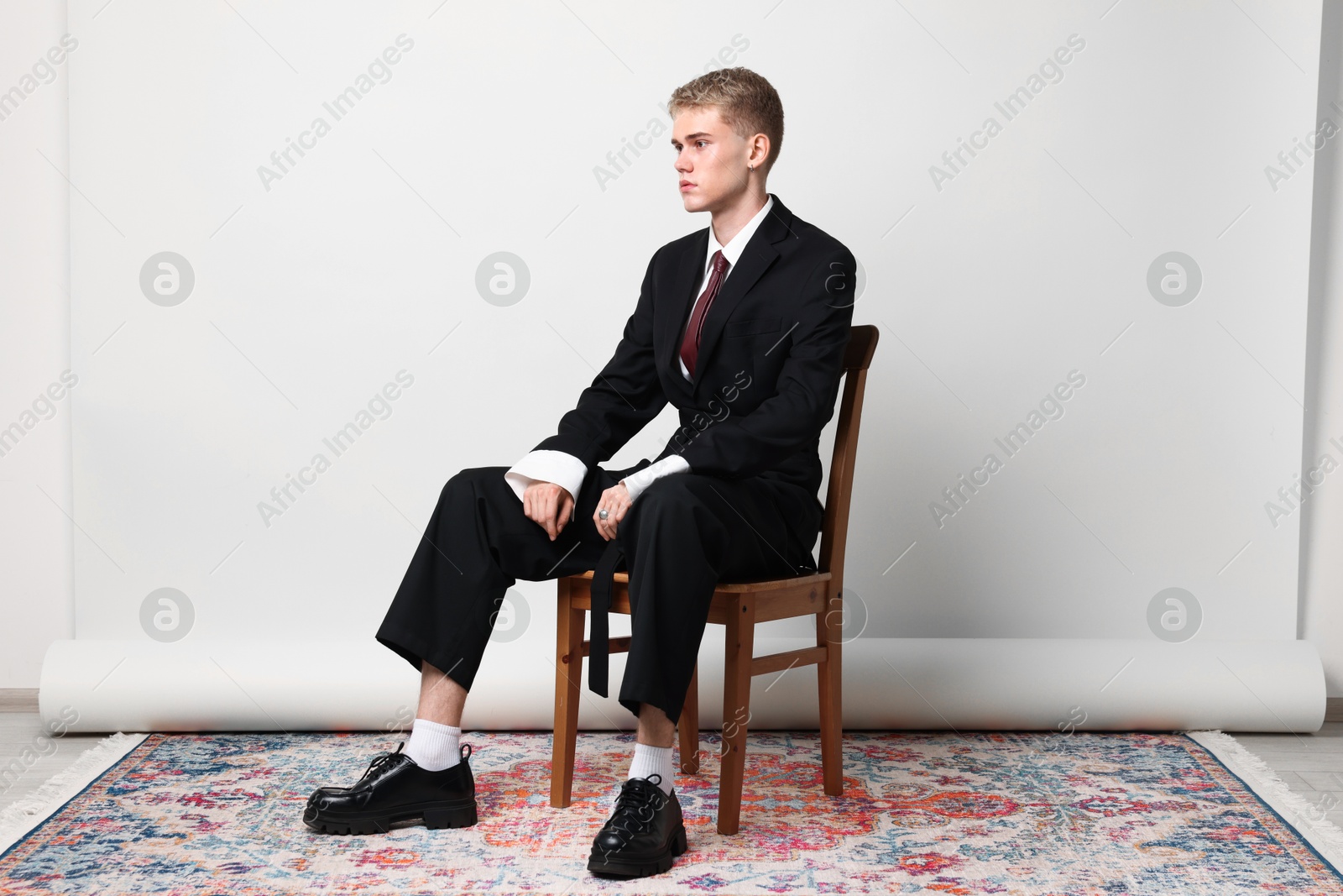 Photo of Handsome young man wearing stylish suit sitting on chair against white background