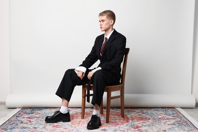 Photo of Handsome young man wearing stylish suit sitting on chair against white background