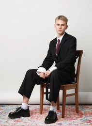 Photo of Handsome young man wearing stylish suit sitting on chair against white background