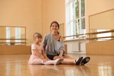 Photo of Little girl and her teacher sitting on floor in barre studio