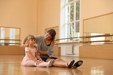 Photo of Little girl and her teacher sitting on floor in barre studio
