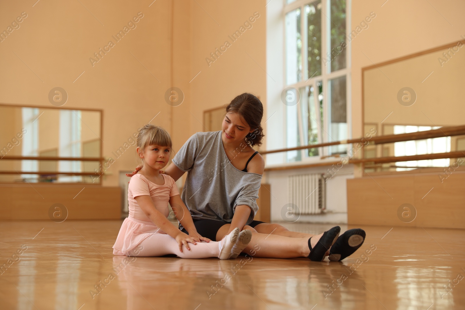 Photo of Little girl and her teacher sitting on floor in barre studio