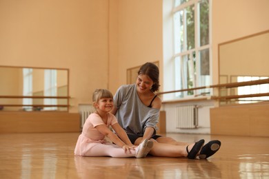 Photo of Little girl and her teacher sitting on floor in barre studio