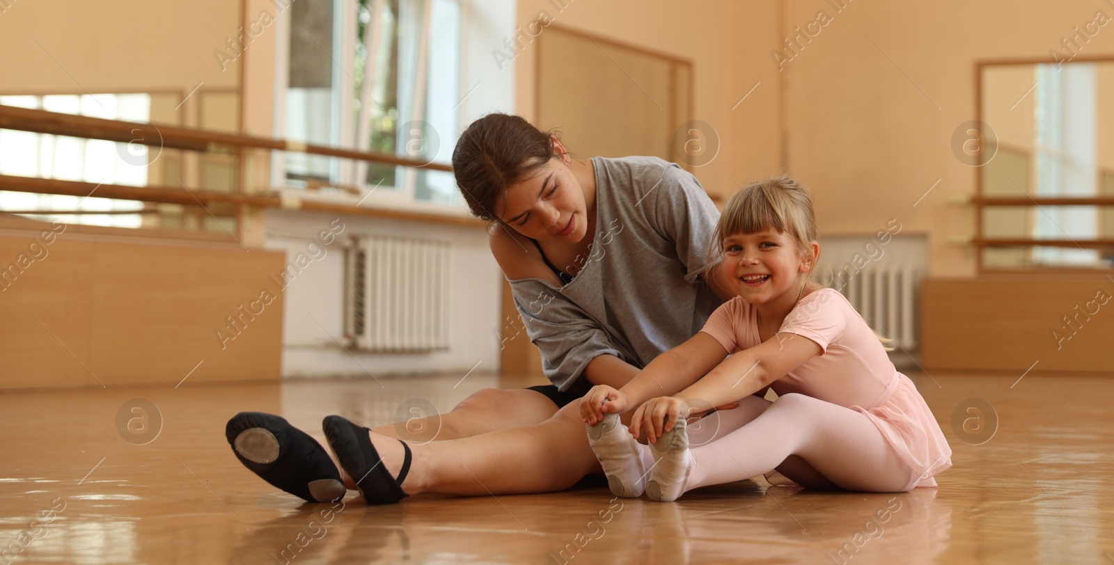 Ballet teacher helping little girl to stretch on floor in dance class Photo of Ballet teacher helping little girl to stretch on floor in dance class