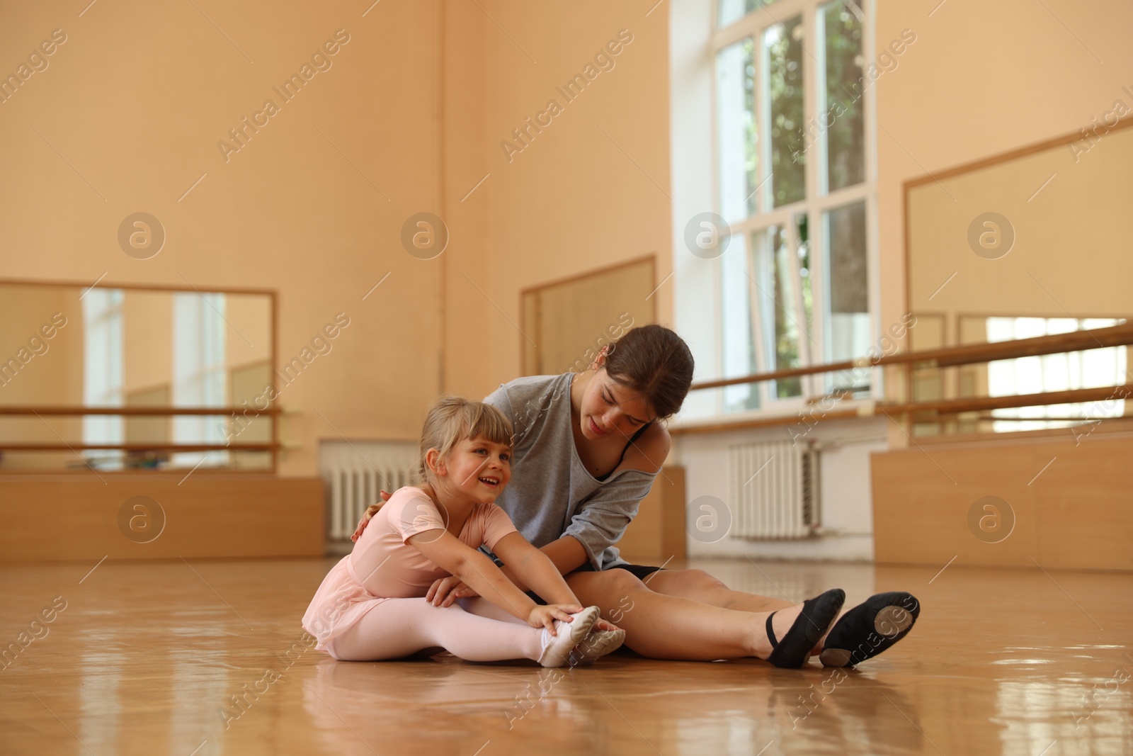 Ballet teacher helping little girl to stretch on floor in dance class Photo of Ballet teacher helping little girl to stretch on floor in dance class