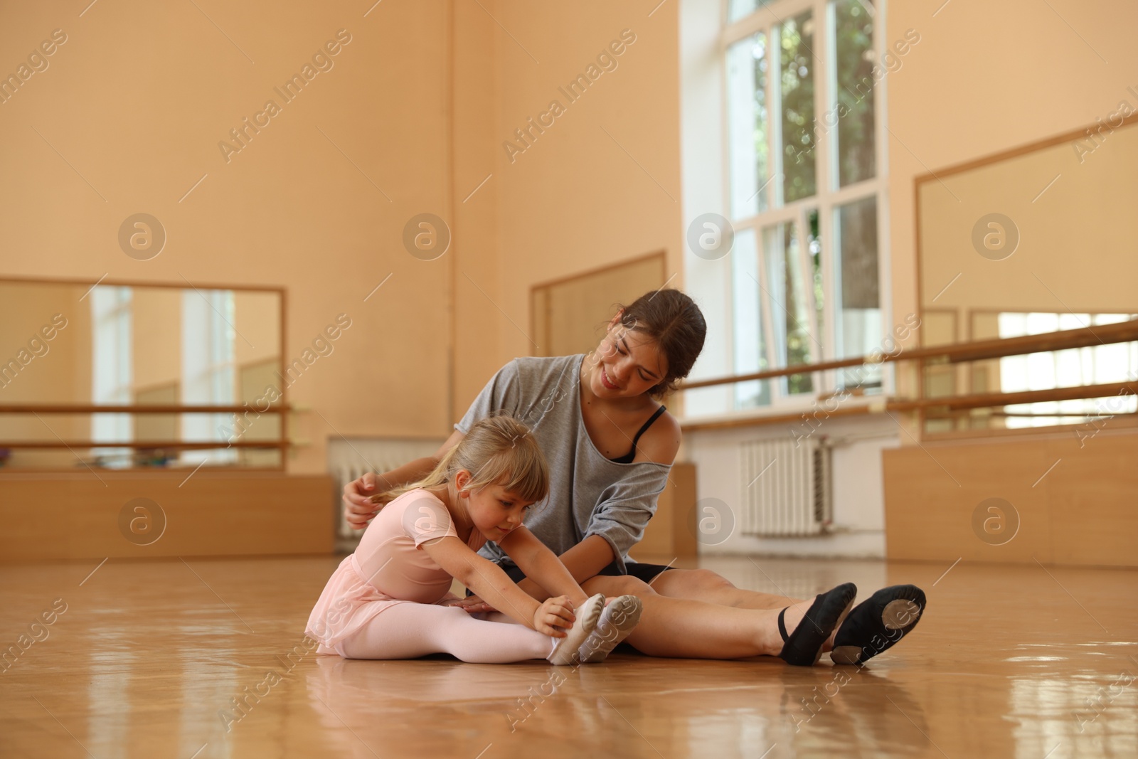 Smiling ballet teacher helping little girl to stretch on floor in dance class Photo of Smiling ballet teacher helping little girl to stretch on floor in dance class