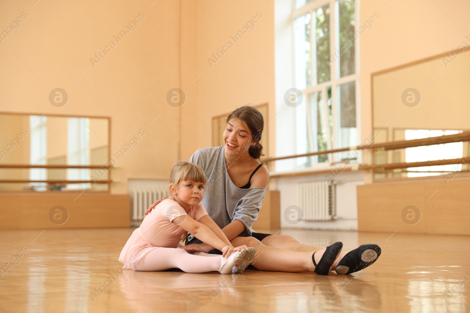 Smiling ballet teacher helping little girl to stretch on floor in dance class Photo of Smiling ballet teacher helping little girl to stretch on floor in dance class