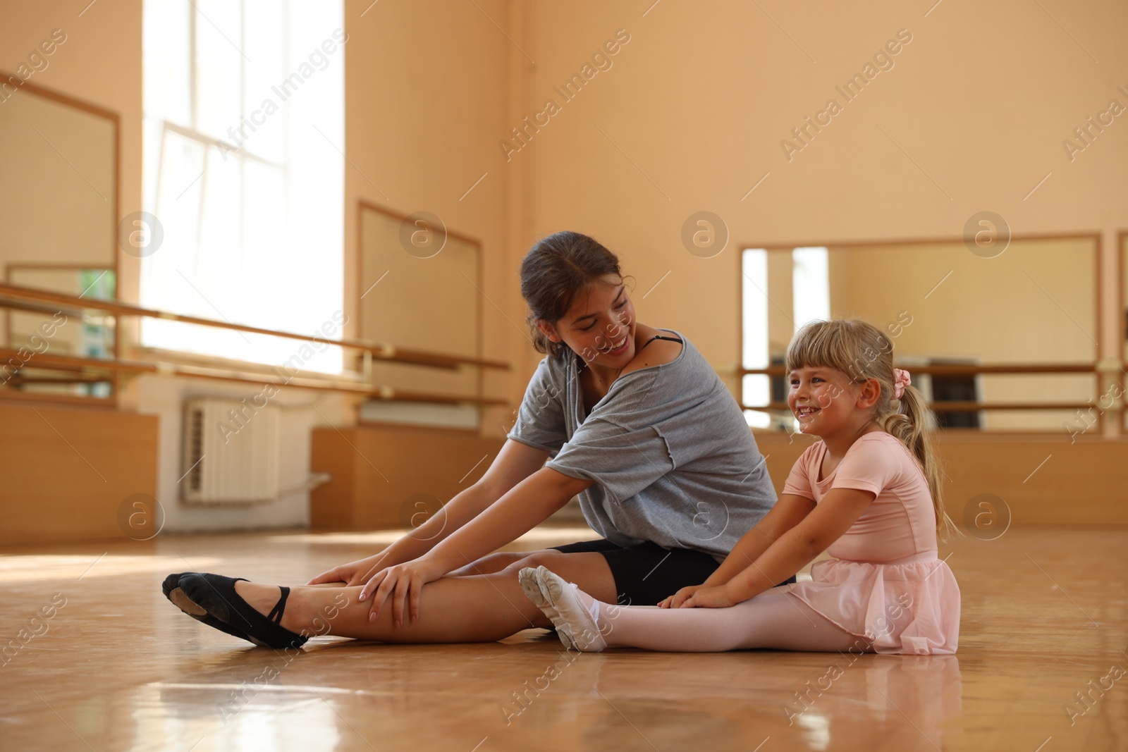 Smiling little girl and her teacher sitting on floor in barre studio Photo of Smiling little girl and her teacher sitting on floor in barre studio