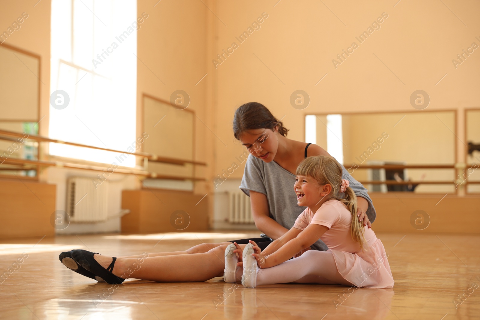 Ballet teacher helping little girl to stretch on floor in dance class Photo of Ballet teacher helping little girl to stretch on floor in dance class