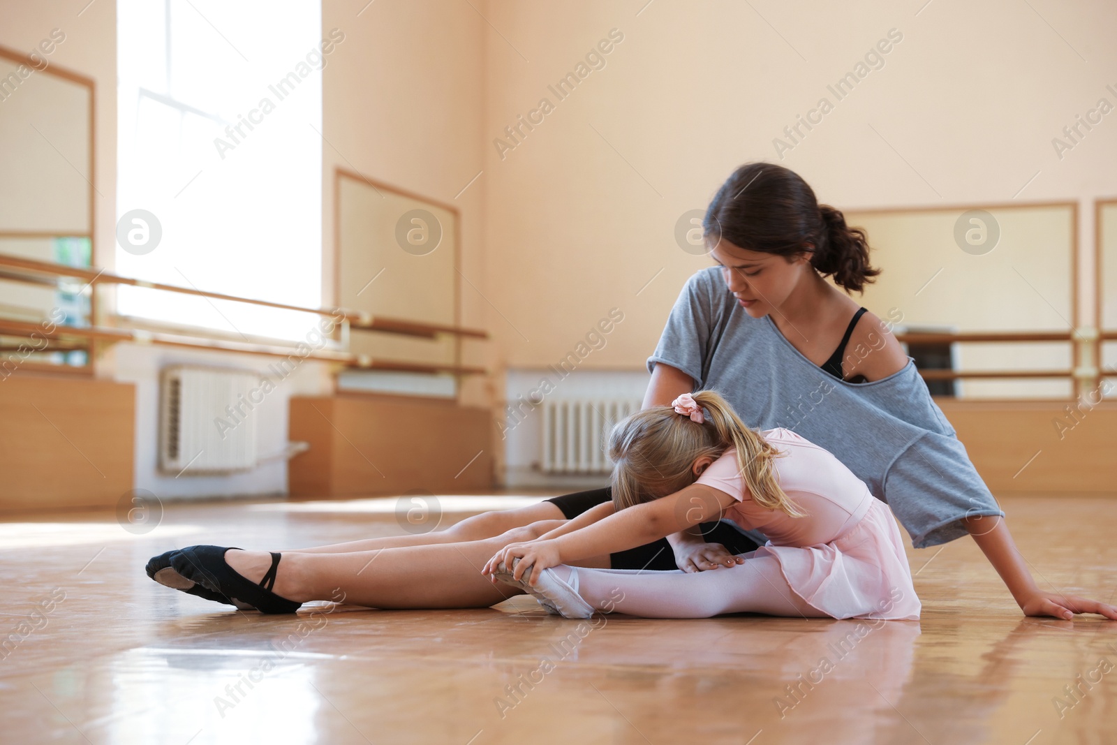 Ballet teacher helping little girl to stretch on floor in dance class Photo of Ballet teacher helping little girl to stretch on floor in dance class