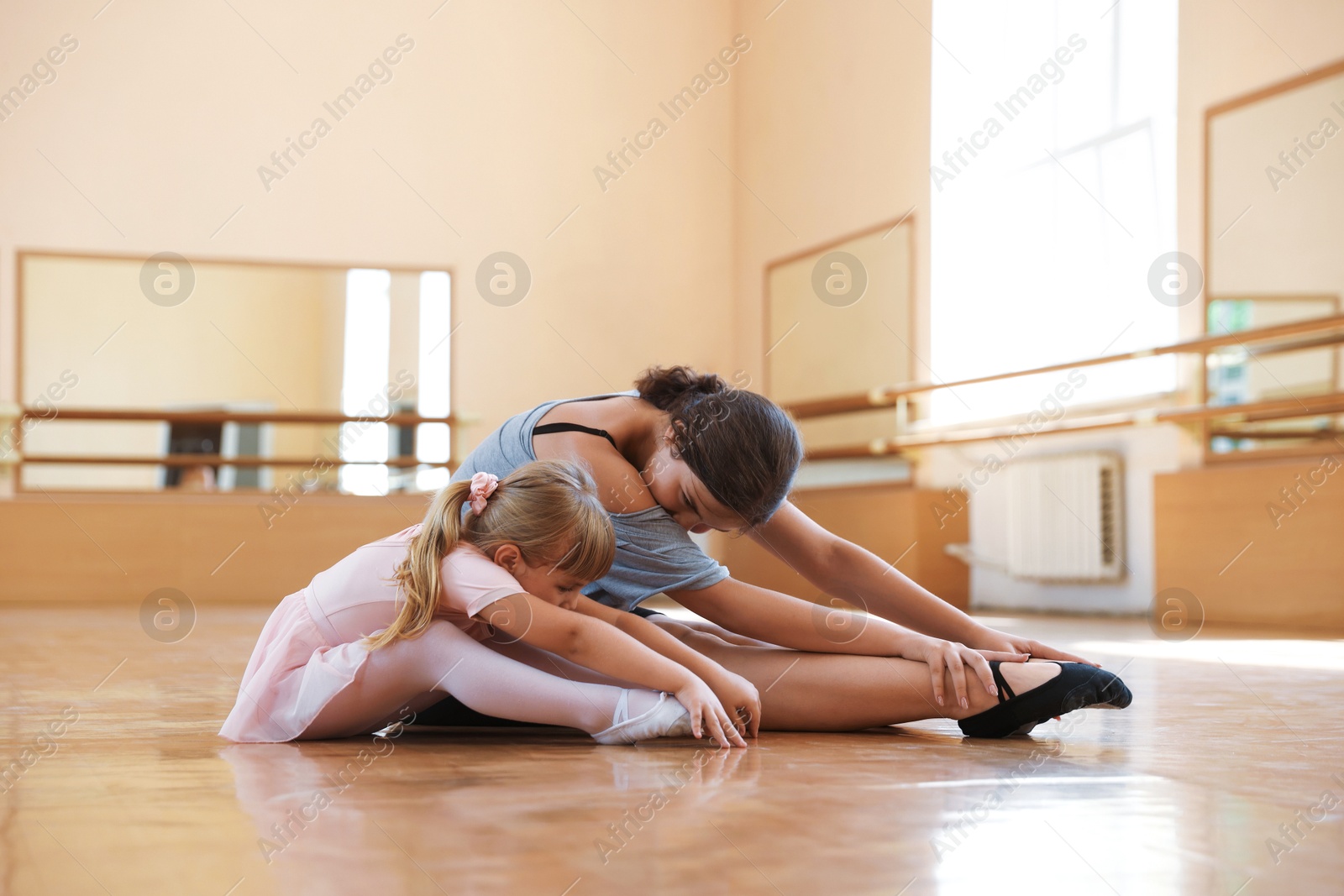 Ballet teacher helping little girl to stretch on floor in dance class Photo of Ballet teacher helping little girl to stretch on floor in dance class