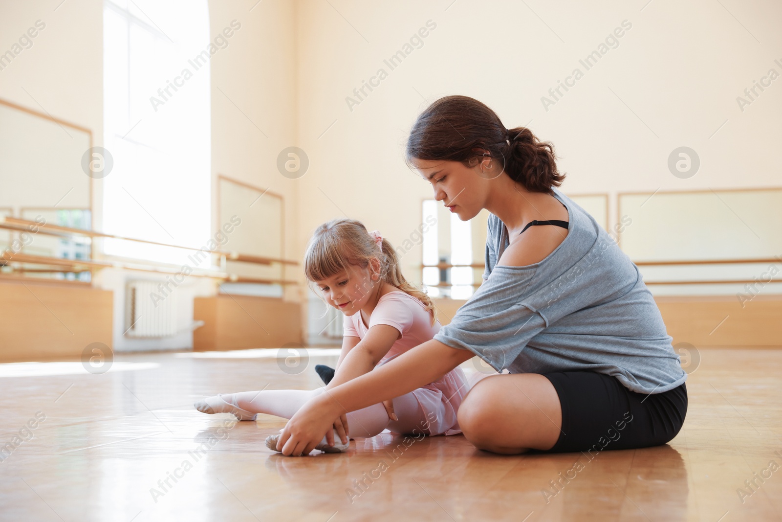 Ballet teacher helping little girl to stretch on floor in dance class Photo of Ballet teacher helping little girl to stretch on floor in dance class