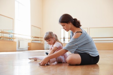 Photo of Ballet teacher helping little girl to stretch on floor in dance class