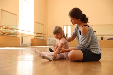Photo of Ballet teacher helping little girl to stretch on floor in dance class