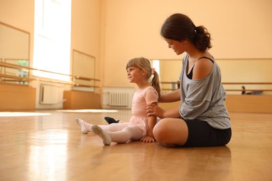 Photo of Ballet teacher working with little girl on floor in dance class