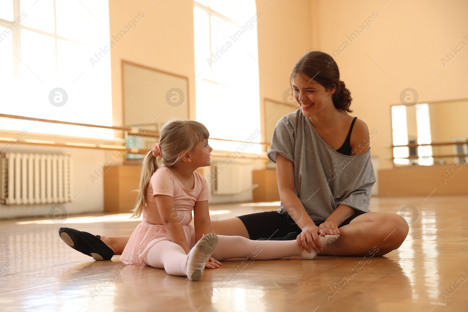 Photo of Happy ballet teacher working with little girl on floor in dance class