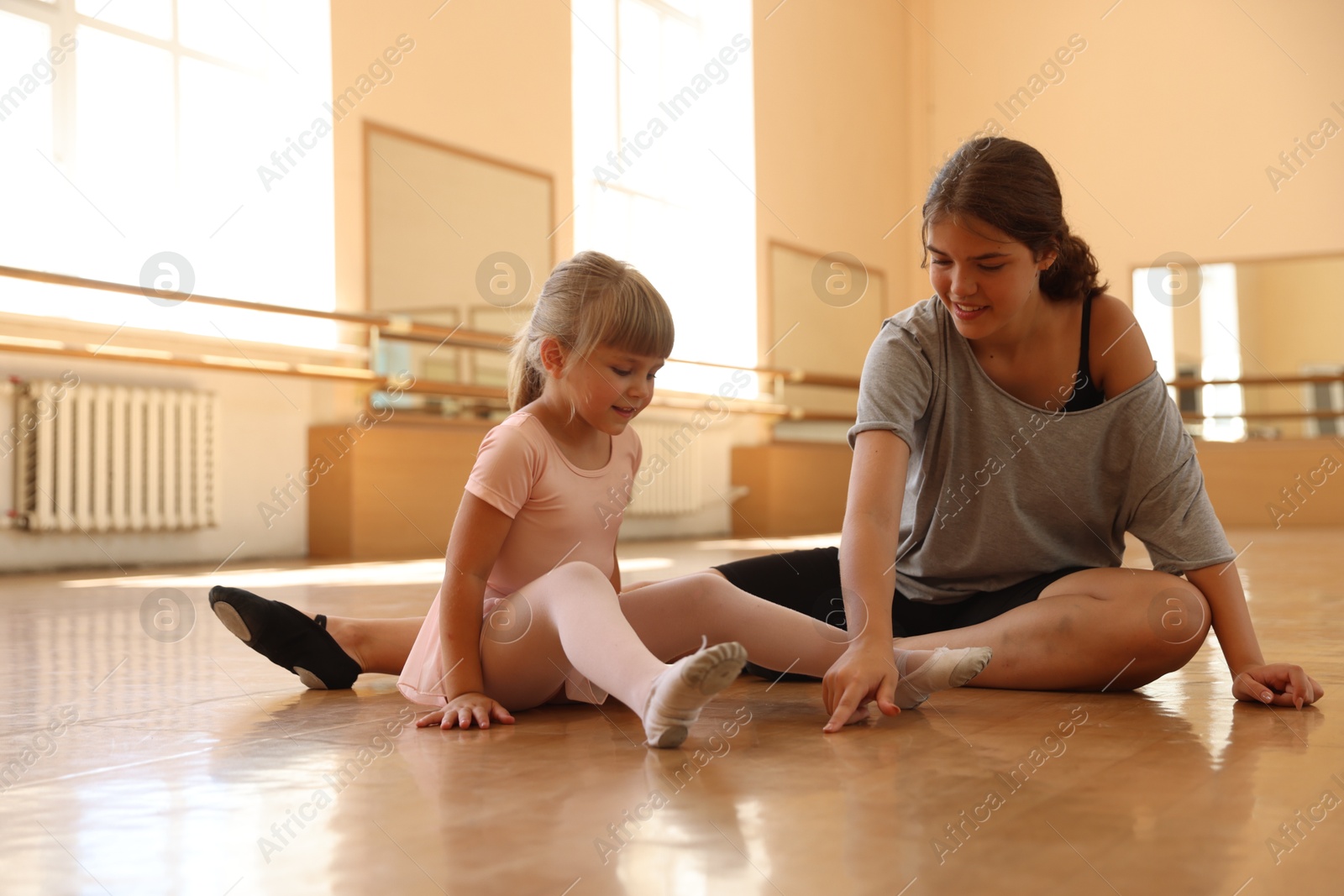Smiling ballet teacher helping little girl to stretch in dance class Photo of Smiling ballet teacher helping little girl to stretch in dance class