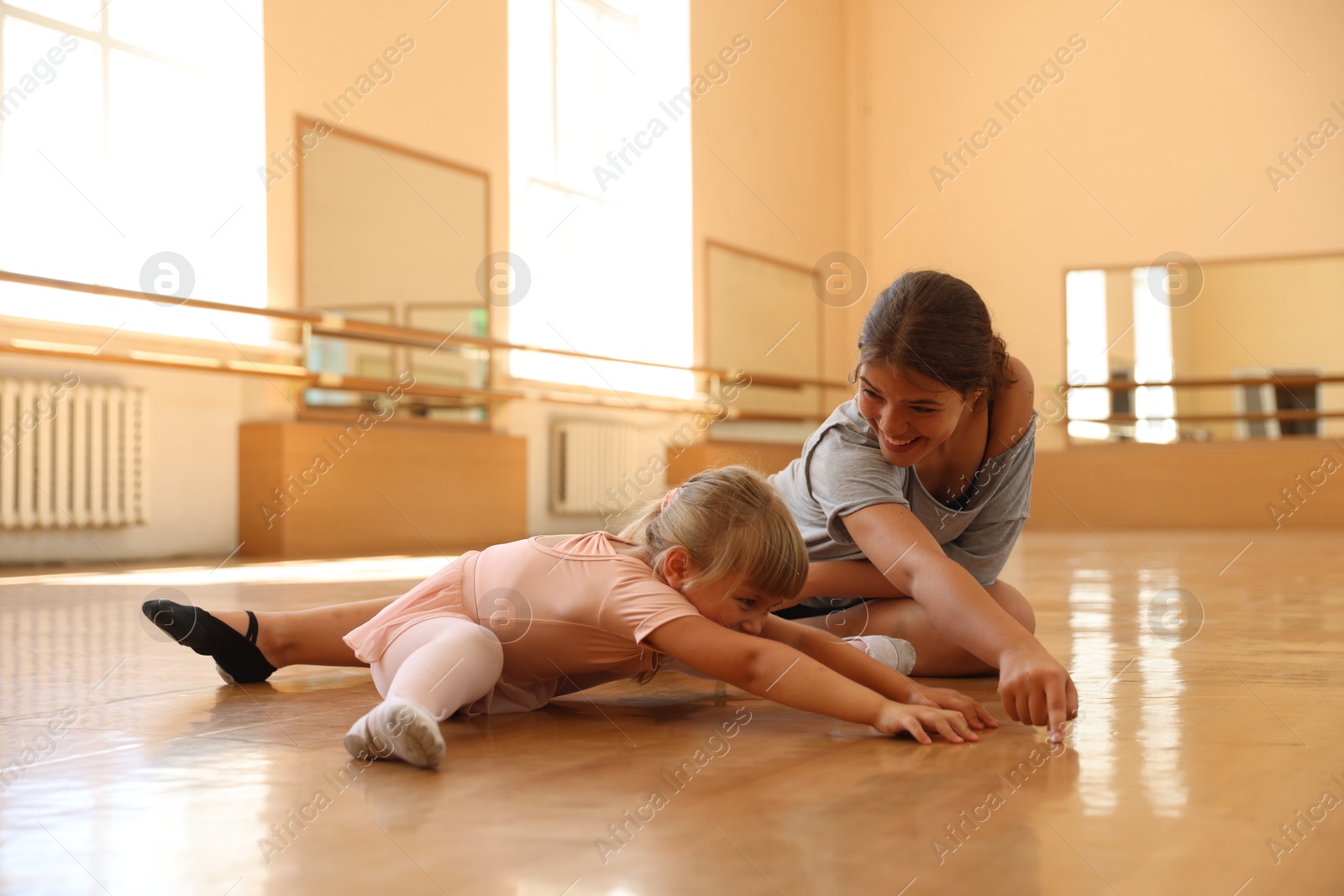 Smiling ballet teacher helping little girl to stretch in dance class Photo of Smiling ballet teacher helping little girl to stretch in dance class
