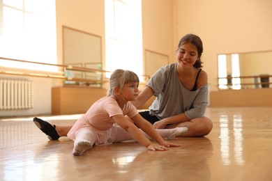 Photo of Smiling ballet teacher helping little girl to stretch in dance class
