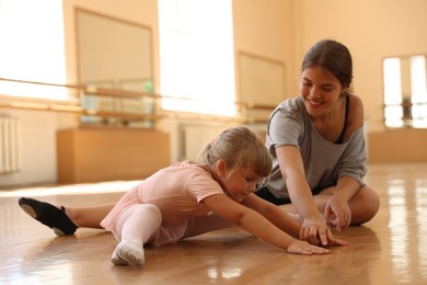 Photo of Smiling ballet teacher helping little girl to stretch in dance class
