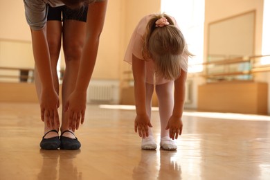 Photo of Ballet teacher stretching with little girl in dance class, closeup