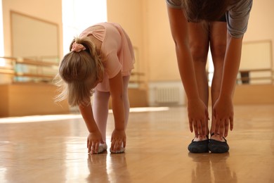Photo of Ballet teacher stretching with little girl in dance class, closeup
