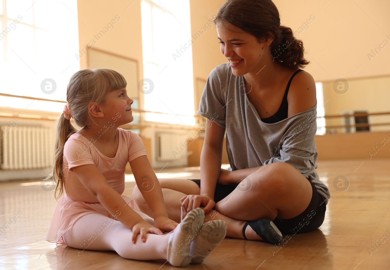 Happy ballet teacher working with little girl on floor in dance class Photo of Happy ballet teacher working with little girl on floor in dance class