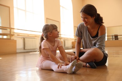 Photo of Happy ballet teacher working with little girl on floor in dance class
