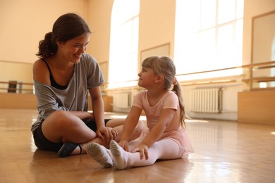 Photo of Happy ballet teacher working with little girl on floor in dance class