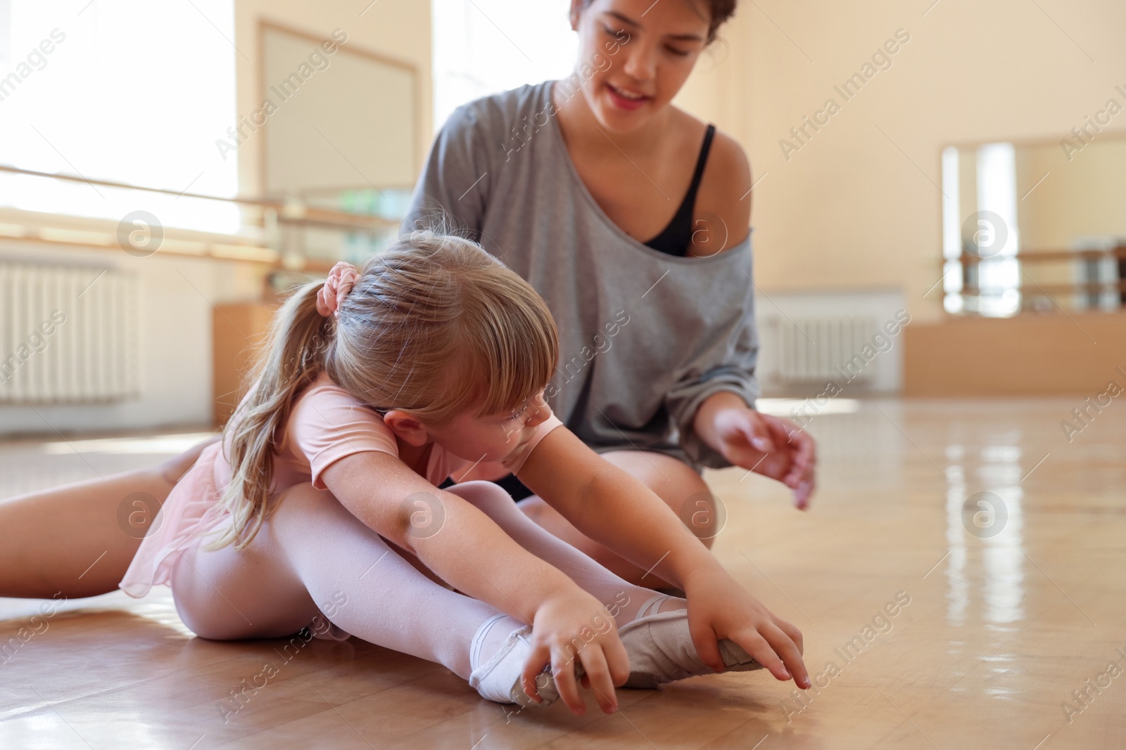 Photo of Ballet teacher working with little girl on floor in dance class