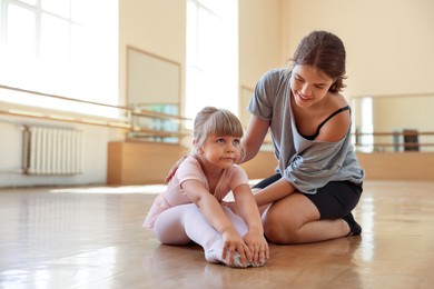 Photo of Smiling ballet teacher helping little girl to stretch in dance class