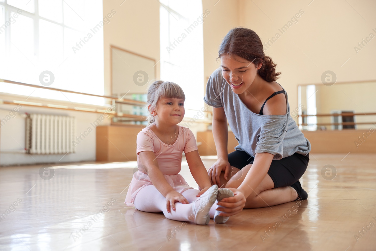 Happy ballet teacher working with little girl on floor in dance class Photo of Happy ballet teacher working with little girl on floor in dance class
